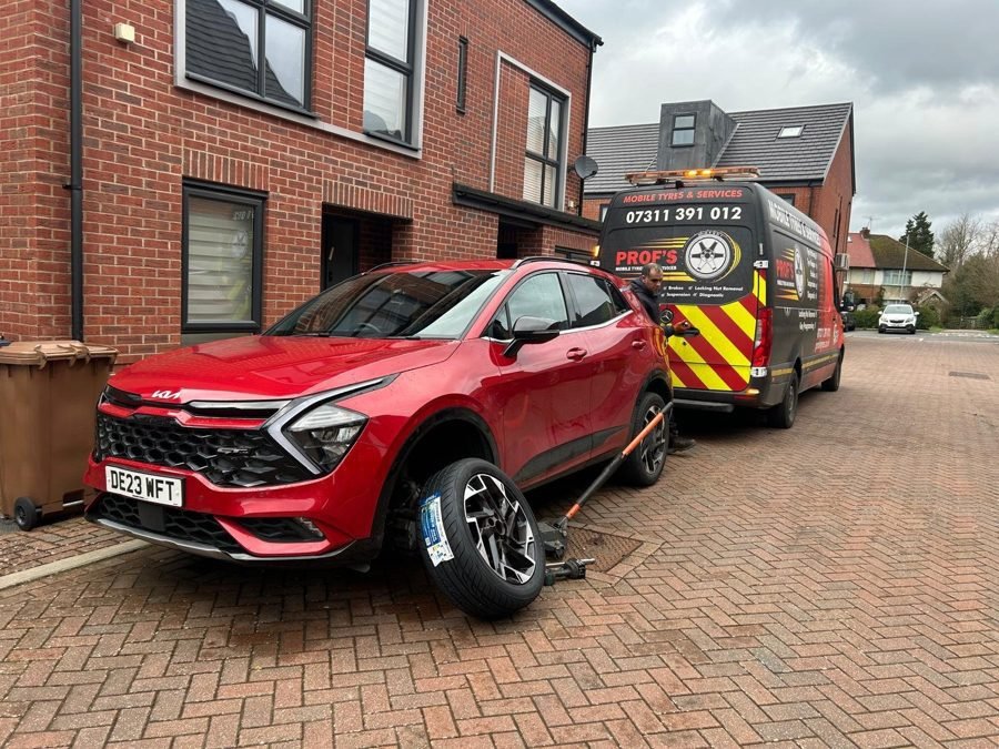 Technician changing a tyre on a red car outside a home, Prof’s van behind