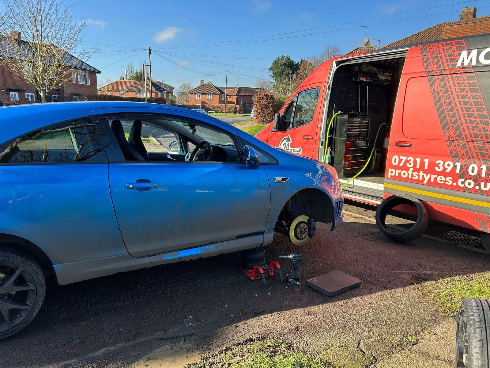 Tyre replacement on a blue car with the Prof's van beside it